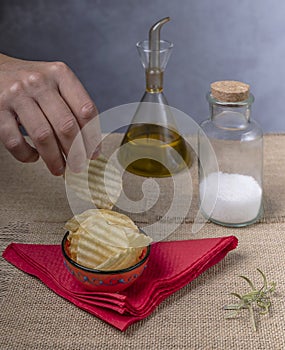 A male hand takes a potato chip from an orange saucer with salt and olive oil nearby