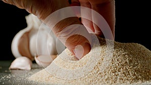 Male hand taking a pinch of white garlic grains by a pile