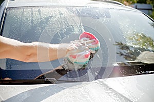 Male hand with tool for washing windows, car wash.man washing a soapy blue car with colorful sponge.Man washing car with