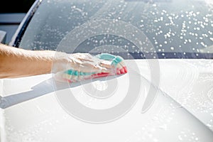 Male hand with tool for washing windows, car wash.man washing a soapy blue car with colorful sponge.Man washing car with