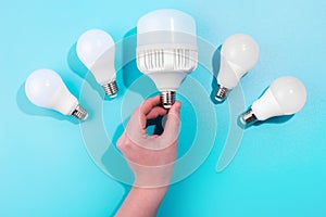 male hand touch big LED light bulbs on blue color background with little led lamps. Flat lay with copy space