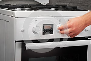 Male hand turning on white kitchen gas stove on gray