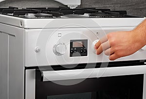 Male hand turning on white kitchen gas stove on gray