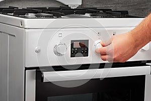 Male hand turning on white stove on gray background