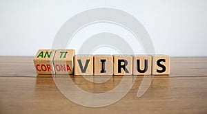 Male hand turns a cube and changes the expression `Corona Virus` to `Anti Virus`. Beautiful wooden table, white background.