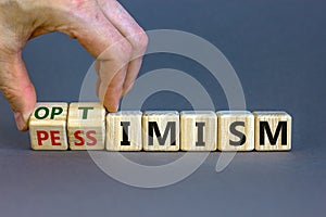 Male hand turns cubes and changes the expression `pessimism` to `optimism`. Beautiful grey background. Business concept. Copy