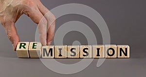 Male hand turns cubes and changes word `mission` to `remission` on a beautiful grey background. Medical, business and covid-19