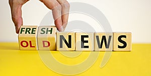 Male hand turns cubes and changes the words `old news` to `fresh news` or vice versa. Beautiful yellow table, white background