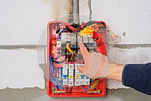 Male hand turns off burning switchboard from overload or short circuit on wall