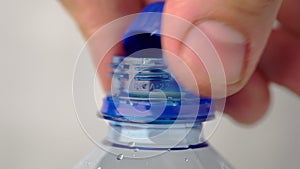 Male hand unscrews and screws cap of a new plastic bottle of carbonated water close up