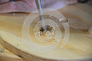 Male hand using a drill bit to drill a hole on plywood.