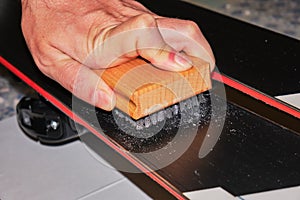 Male hand using a Stainless Steel brush to clean and open the structure of a ski base. Ski tuning and maintenance tool