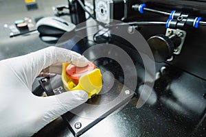 Male hand wearing gloves presses an emergency button of an industrial machine