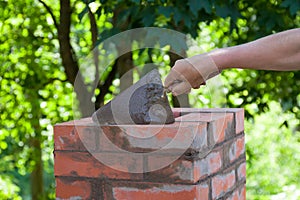 Male hand working with a trowel, repairing a chimney from red bricks on a roof