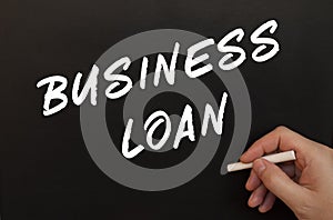 Male hand writes in chalk the words BUSINESS LOAN on a black board
