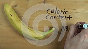 Male hand writes down caloric content of banana on wooden surface