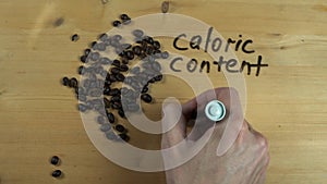 Male hand writes down caloric content of coffee beans on wooden surface