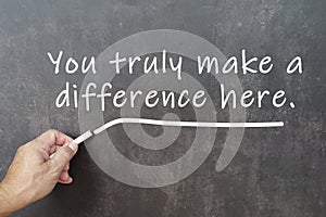 Male hand writes in white chalk pencil the word you truly make a difference here