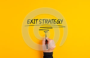 Male hand writing exit strategy on yellow background. Business exit strategy plan or management