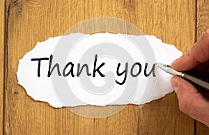 Male hand writing `thank you` on white paper on wooden table. Business concept