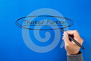 Male hand writing a Trusted partner sign with black marker over blue background