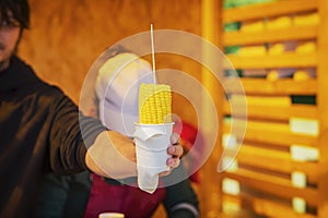 Male hand of young man seller with cooked sweet corn grill