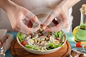 Male hands adds pieces of canned tuna in the bowl with other fresh ingredients.