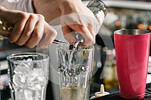 Male hands of the bartender close-up, makes a cocktail on the bar, glasses with ice