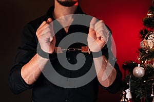 male hands in BDSM handcuffs for submission and domination against the background of a Christmas tree on New Year& x27;s