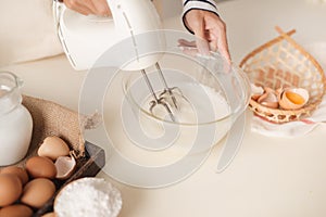 Male hands beating egg whites cream with mixer in the bowl