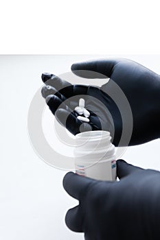 Male hands in black medical gloves put white pills in a plastic bottle