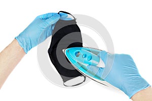 Male hands in blue disposable nitrile gloves iron a black reusable face mask. Washable cloth mask sanitation. First person view