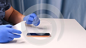 Male hands in blue gloves replaces a broken tempered glass screen protector for a smartphone. A man prepares a