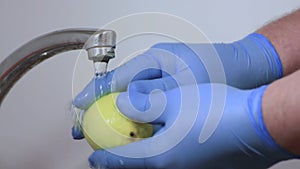 Male hands in blue gloves are washing a yellow lemon with a brush.