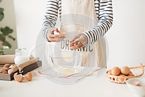 Male hands are breaking an egg into bowl to make dough on white table