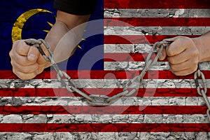 male hands breaking iron chain  symbol of tyranny  protest against the background of the national flag of Malaysia  the