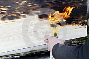 Male hands burning wooden desk, table, surface with burner, woodburning handcraft outside. Close up man holding gas