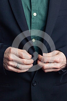 Male hands of a businessman in a business suit with a ring on his finger fasten a button on a jacket. Vertical orientation photo,