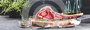 Male hands of butcher or cook holding tomahawk beef steak on dark rustic kitchen table background photo