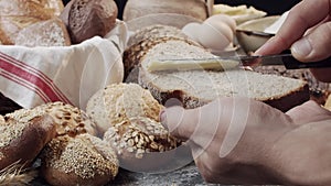 Male hands butter a piece of fresh baked Dutch bread above the wooden table