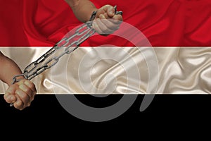 Male hands chained in iron chains against the background of the silk national flag of yemen, concept of protest, crime ban, close-
