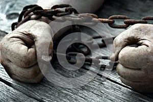 Male hands chained with old rusty chain on the wooden boards.