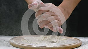 Male hands of the Chef in white flour clap their hands on a black background, close-up