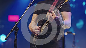 Male hands close up playing bass guitar at concert. Man with guitar in his hands on stage