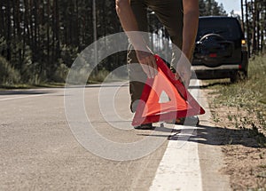 Male hands closeup putting red triangle caution sign on road side near broken car in summer