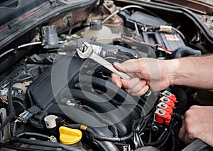 Male hands with combination spanner over the open car bonnet, close up, selective focus