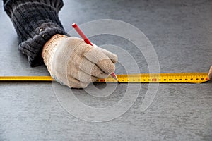 Male hands of  construction worker wearing special gloves measure the details with  construction tape and mark the construction