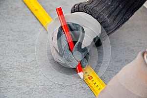 Male hands of  construction worker wearing special gloves measure the details with  construction tape and mark the construction