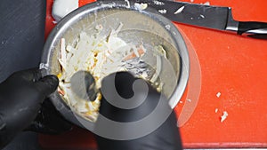 Male hands of cook in gloves stirring ingredients in iron bowl using a spoon. Arms of chef mixing mayonnaise with