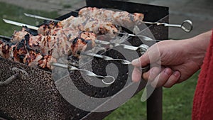 Male hands cook shish kebab on grill outside.